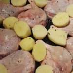 Duck legs with potatoes on a baking sheet before baking